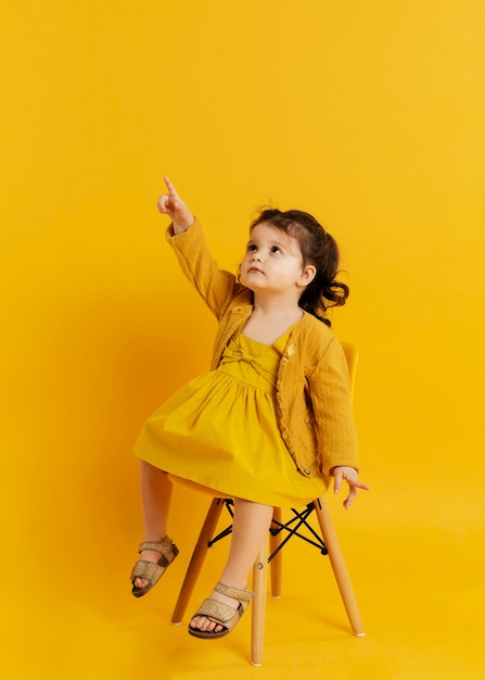 Front view of child posing while sitting on chair and pointing up