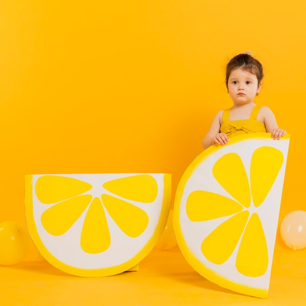 Вид спереди ребенка позирует с украшениями ломтиками лимона