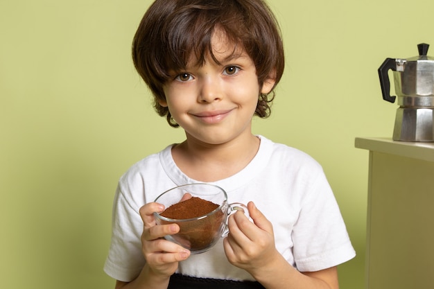 A front view child smiling boy adorable in white t-shirt holding powdered coffee on the stone colored space