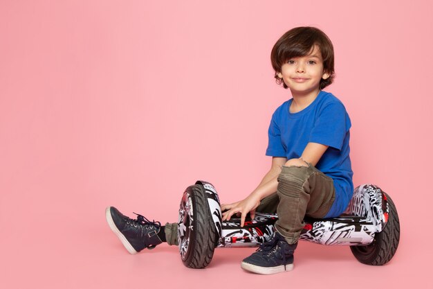A front view child smiling boy in blue t-shirt sitting on the segway on the pink space