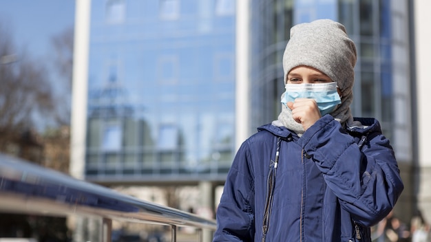 Front view of child wearing medical mask and coughing