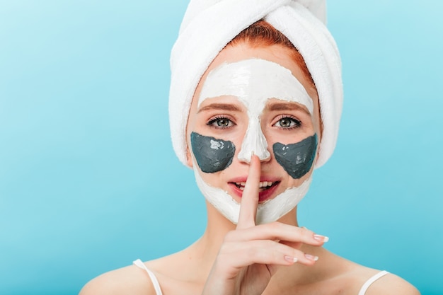 Front view of chilling lady with face mask showing silence sign. Studio shot of relaxed female model with towel on head isolated on blue background.