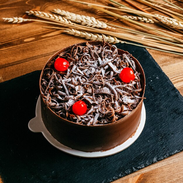 A front view choco cake decorated with chocolate cream red cherries inside brown cake pan celebration delicious birthday on the brown background