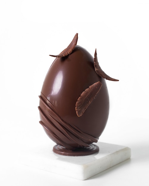 Vista frontale uovo di cioccolato disegnato con garbo sulla scrivania bianca