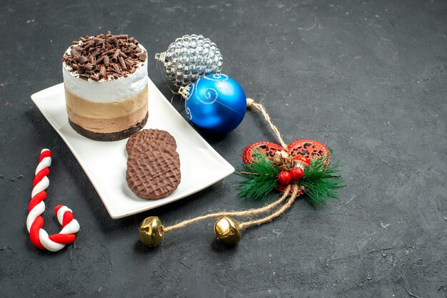 Front view chocolate cake and biscuits on white rectangular plate colorful xmas tree toys on dark isolated background free place