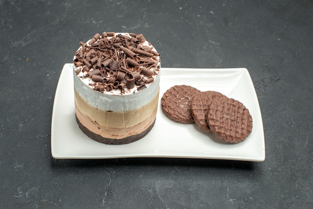 Front view chocolate cake and biscuits on white rectangular plate on dark