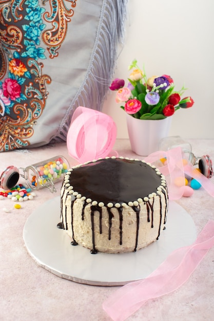 A front view chocolate cake with candies on the pink desk