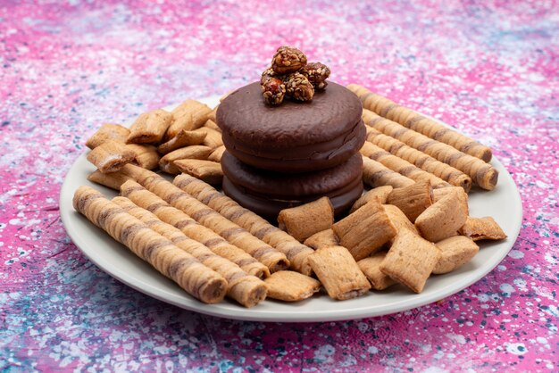 Front view of chocolate cakes with cookies inside plate on the purple surface