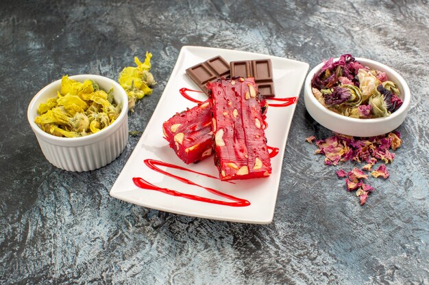 Front view of chocolate on white plate with bowls of dry flowers on grey ground