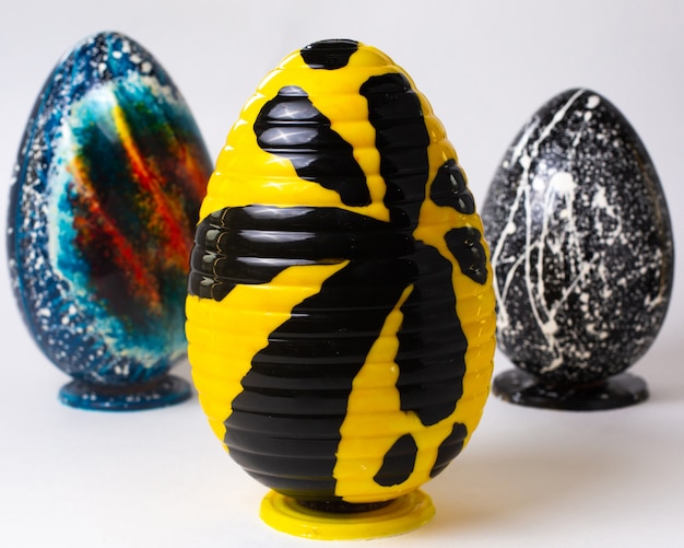 Front view chocolate yellow egg with a black hieroglyph on stand with two other chocolate eggs