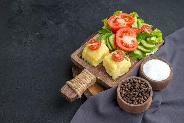 まな板の上に刻んだ新鮮な野菜のチーズと黒い表面に濃い色のタオルにスパイスを置いた正面図
