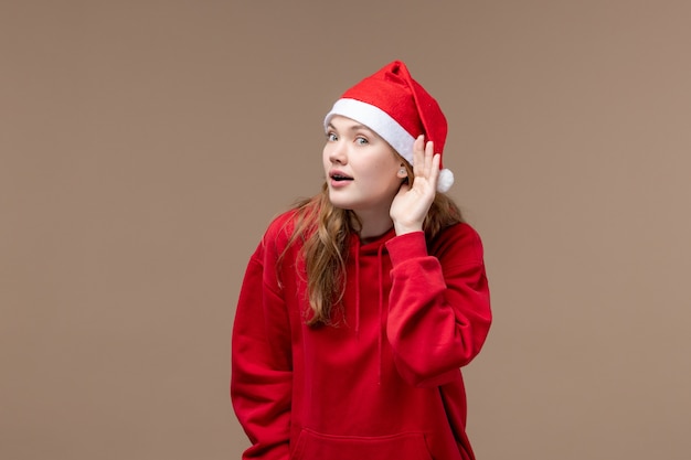 茶色の背景の休日のクリスマスの感情に注意深く耳を傾けようとしている正面のクリスマスの女の子