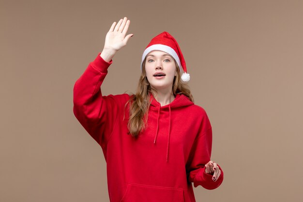 正面図のクリスマスの女の子が茶色の背景に手を振っている女性の休日のクリスマス