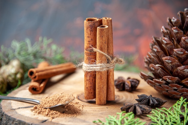 Front view cinnamon sticks cinnamon powders pinecone anises on wood board on dark background