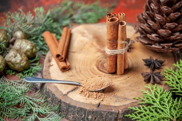 Front view cinnamon sticks cinnamon powders pinecone anises on wood board spoon with cinnamon powder on dark