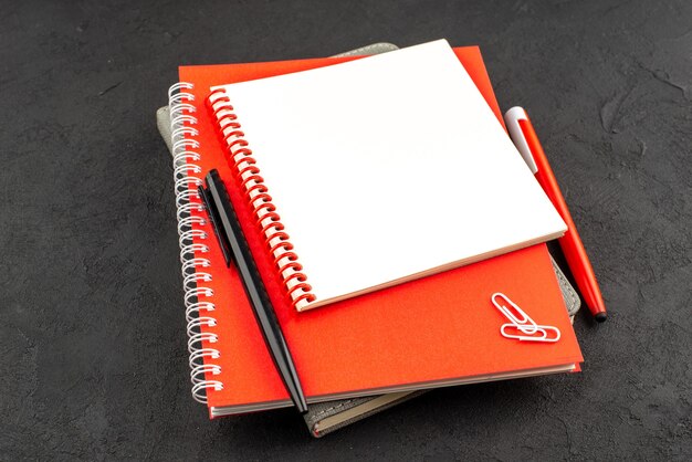 Front view of closed spiral notebooks in different sizes and pens on black