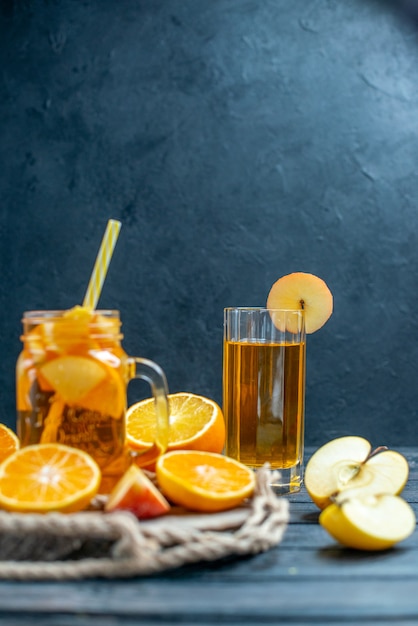 Бесплатное фото Апельсины и яблоки нарезанные спереди коктейль на деревянной доске на темном изолированном фоне