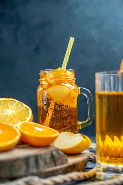 Front view cocktail cut oranges and apples on wood board on dark isolated background