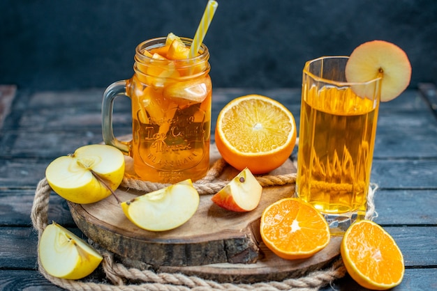 Front view cocktail cut oranges and apples on wood board on dark isolated background