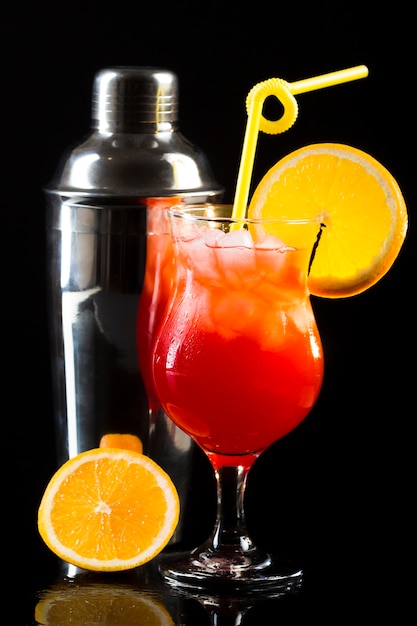 Front view of cocktail shaker and glass with orange and straw