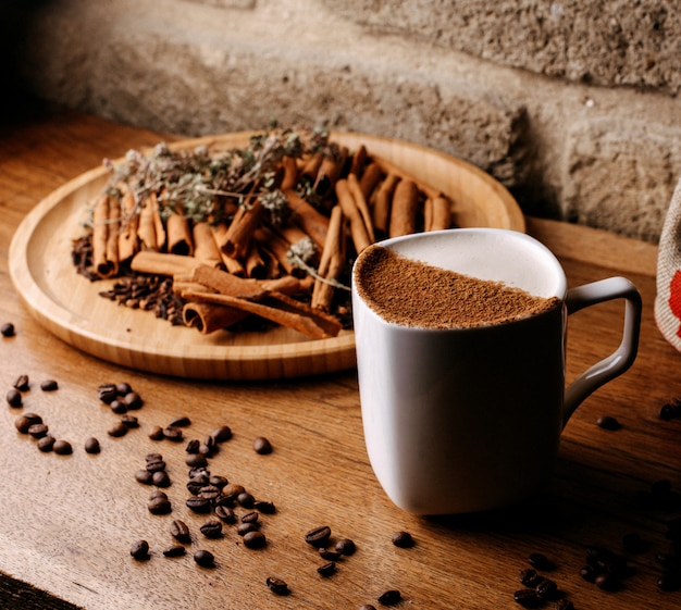 Вид спереди кофе внутри белой чашки вместе с семенами кофе и корицей