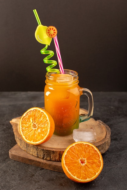 A front view cold cocktail colored inside glass can with colorful straw with ice cubes oranges isolated on the wooden desk and dark