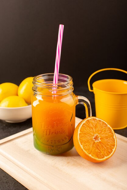 A front view cold cocktail colored inside glass cans with colorful straw lemons flowers on the wooden cream desk and dark