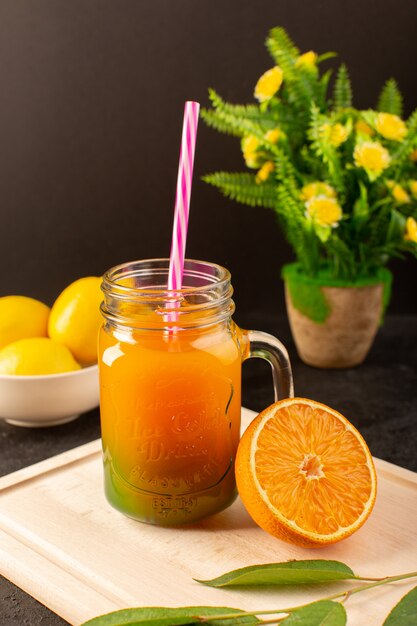 Foto gratuita un cocktail freddo vista frontale colorato all'interno di lattine di vetro con limoni di paglia colorati foglie verdi sulla scrivania in legno crema e buio