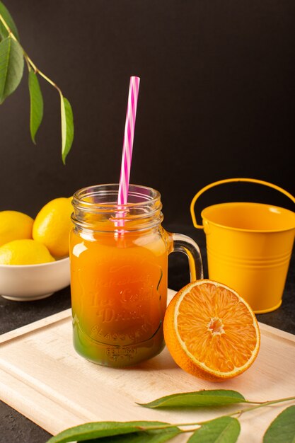 A front view cold cocktail colored inside glass cans with colorful straw lemons green leaves on the wooden cream desk and dark