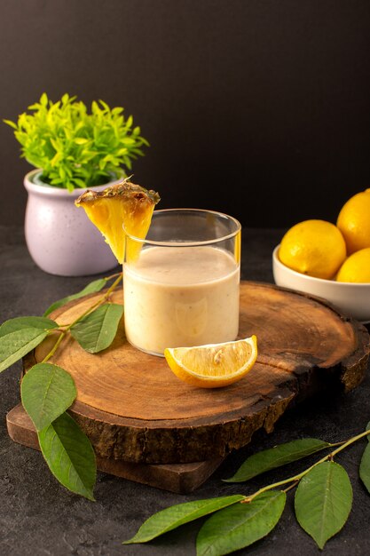 A front view cold cocktail colored inside glass with green leaves and with lemons little plant isolated on the dark