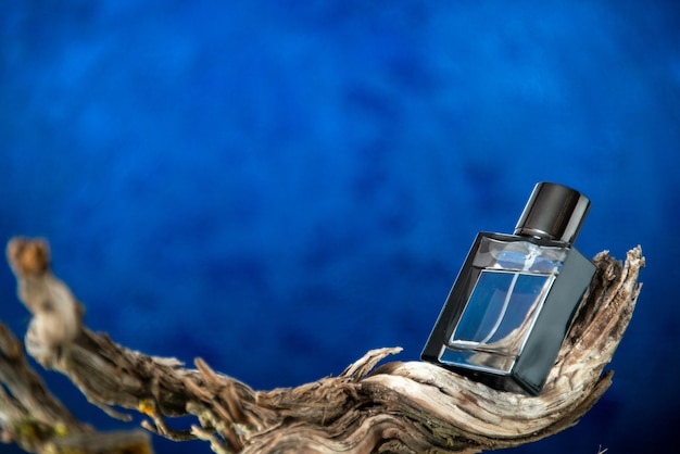 Бесплатное фото Вид спереди бутылка одеколона на ветке гнилого дерева на темно-синем фоне