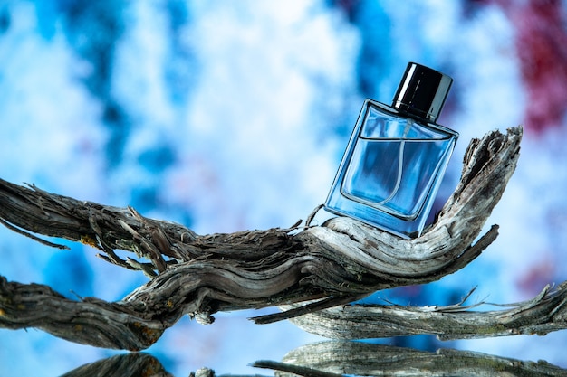 Free photo front view of cologne bottle on rotten tree branch on blue abstract background