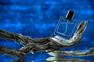 Free photo front view cologne bottle on rotten tree branch on dark blue background