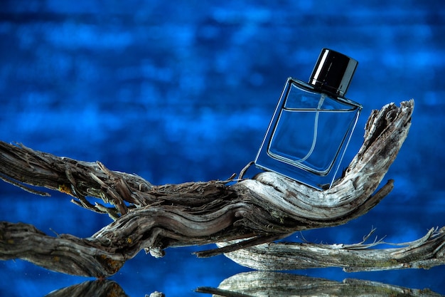 Front view cologne bottle on rotten tree branch on dark blue background