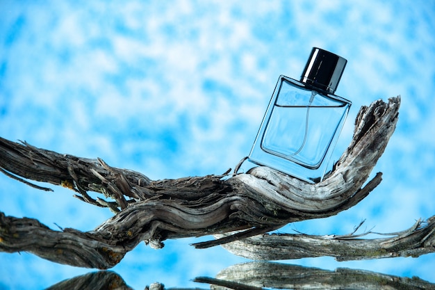Вид спереди бутылка одеколона на гнилой ветке дерева на светло-синем фоне