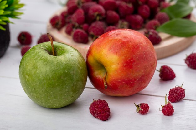 Front view of colored apples with raspberries on a white surface