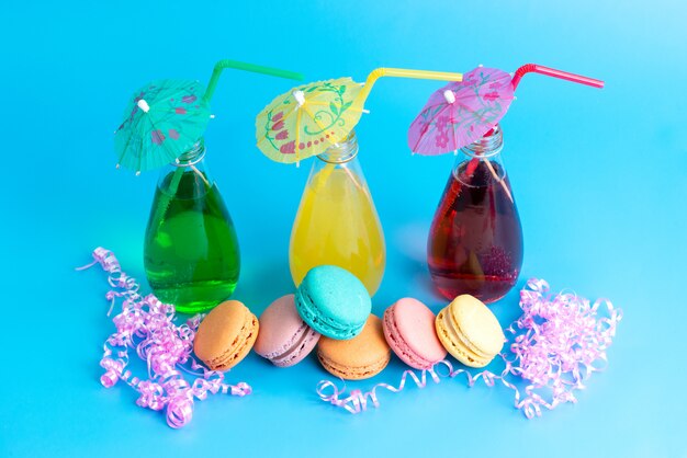 A front view colored cocktails with straws along with french macarons on blue