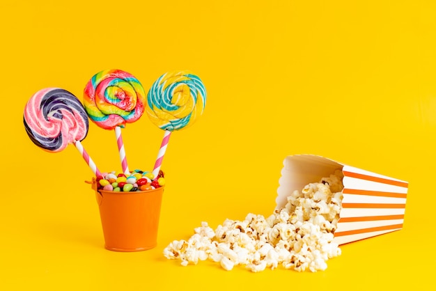 A front view colored lollipops with colorful candies and popcorn on yellow