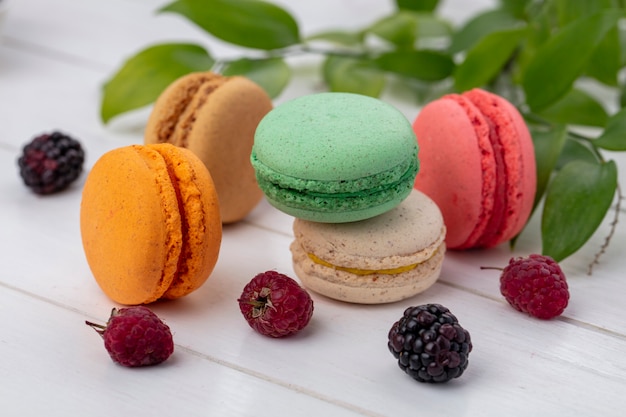 Front view of colored macarons with blackberries and raspberries on a white surface