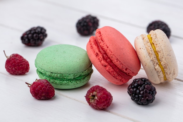 Front view of colored macarons with blackberries and raspberries on a white surface