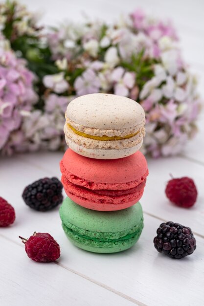 Front view of colored macarons with blackberries and raspberries on a white surface