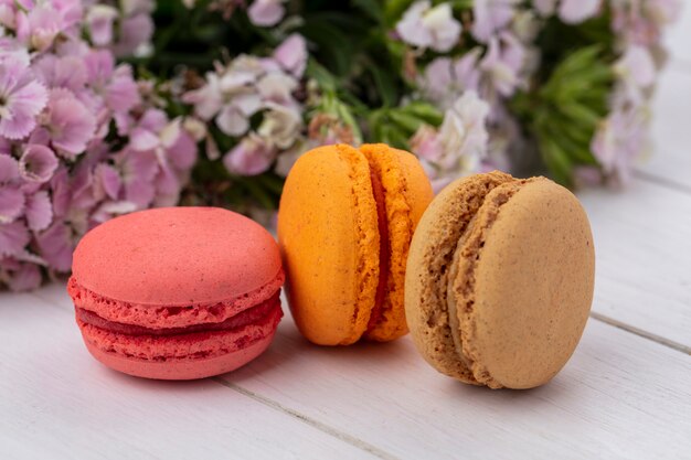 Front view of colored macarons with flowers on a white surface