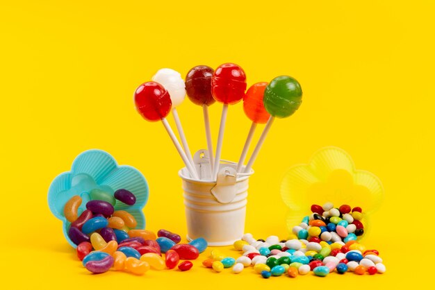 A front view colorful candies along with lollipops isolated on yellow, sweet sugar color