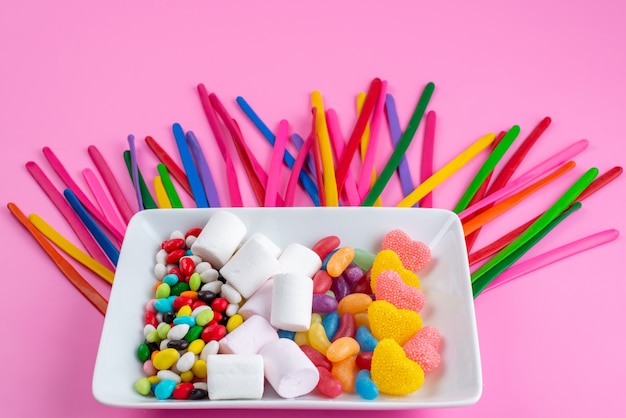 A front view colorful candies along with marshmallows and marmalades on pink, candy color sugar