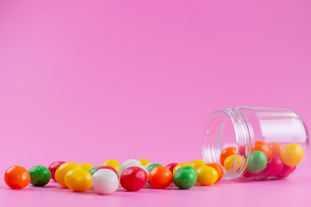 Вид спереди красочные конфеты внутри и снаружи маленькой баночки на розовом, цветном сладком сахаре