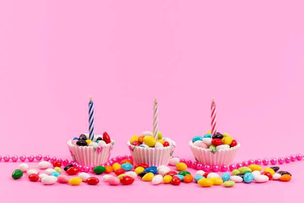 Free photo a front view colorful candies inside white, paper packages with candles oon pink, candy sugar sweet