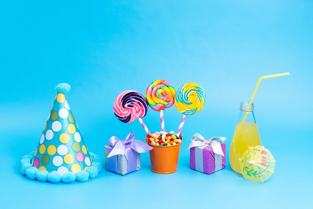 Вид спереди разноцветных конфет с радужными леденцами и маленькими подарочными коробками для коктейля на синем фоне