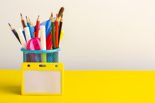 Вид спереди красочные разные карандаши с фломастерами на светло-желтом столе