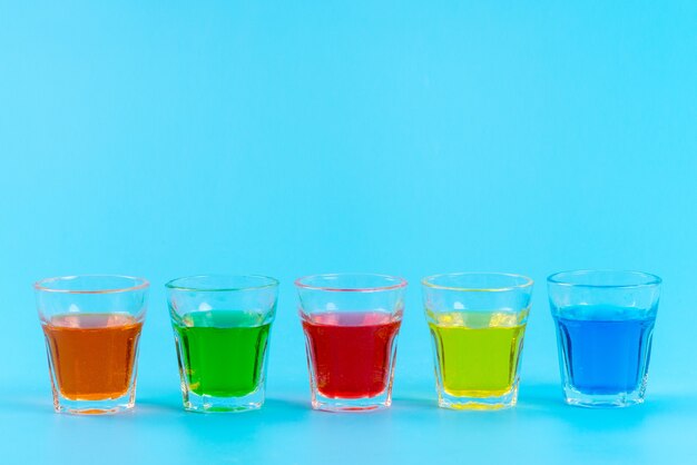 A front view colorful drinks inside glasses cooling on blue, juice fruit color ice