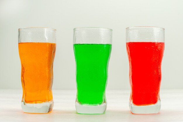 Front view colorful juices inside long glasses on white surface